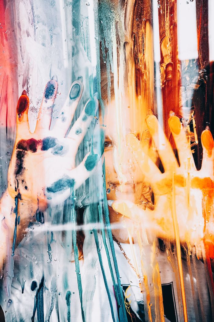 Colorful paint-smeared hands pressing against a glass, creating a striking abstract pattern.