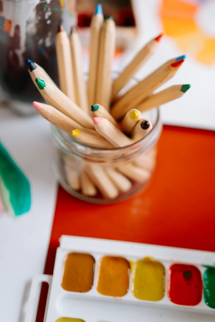 A close-up view of wooden colored pencils in a jar alongside watercolor paints for artistic projects.
